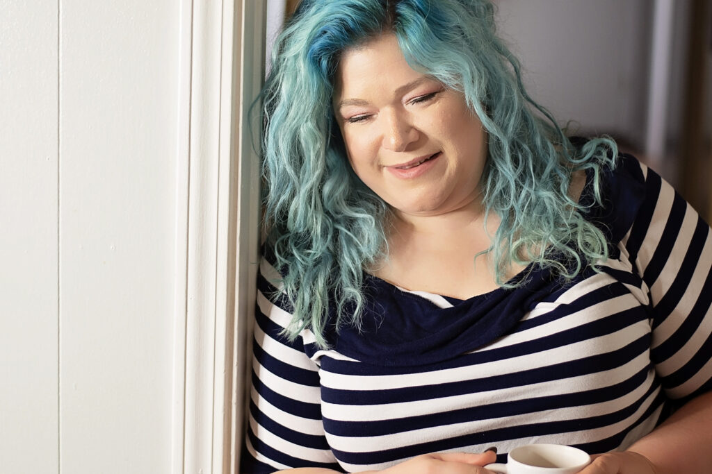 Sarah Bridger leaning in a doorway with a cup of coffee